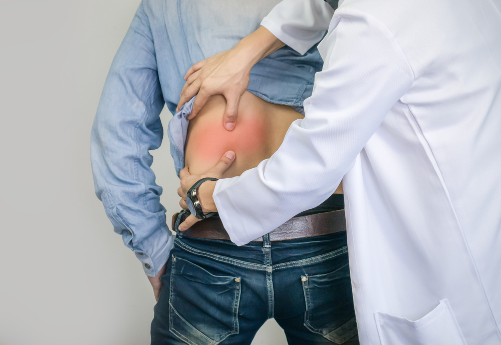 Doctor in white coat palpating and examining male patient's lower back with visible red inflammation mark, assessing pain during clinical evaluation for workplace or occupational injury