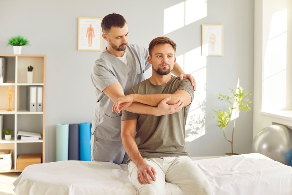 Chiropractor performing manual shoulder and arm adjustment on male patient during physical therapy session in Yonkers clinic