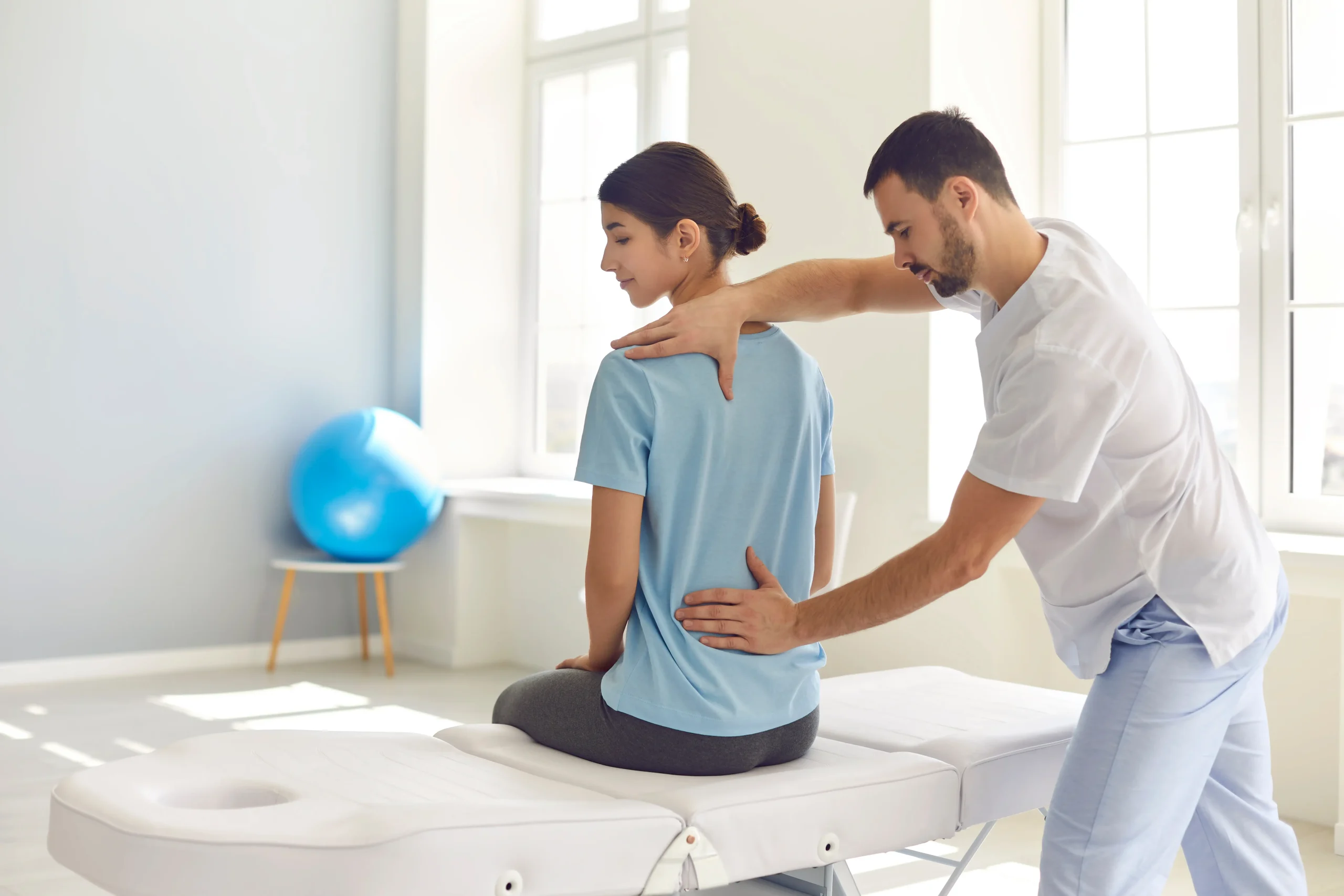 Licensed osteopath examining a woman’s spine during a musculoskeletal evaluation in a clinic office.